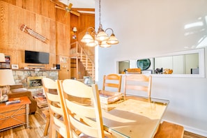 Un'ampia zona living con pavimento in legno, un tavolo da pranzo in vetro e una TV a parete.