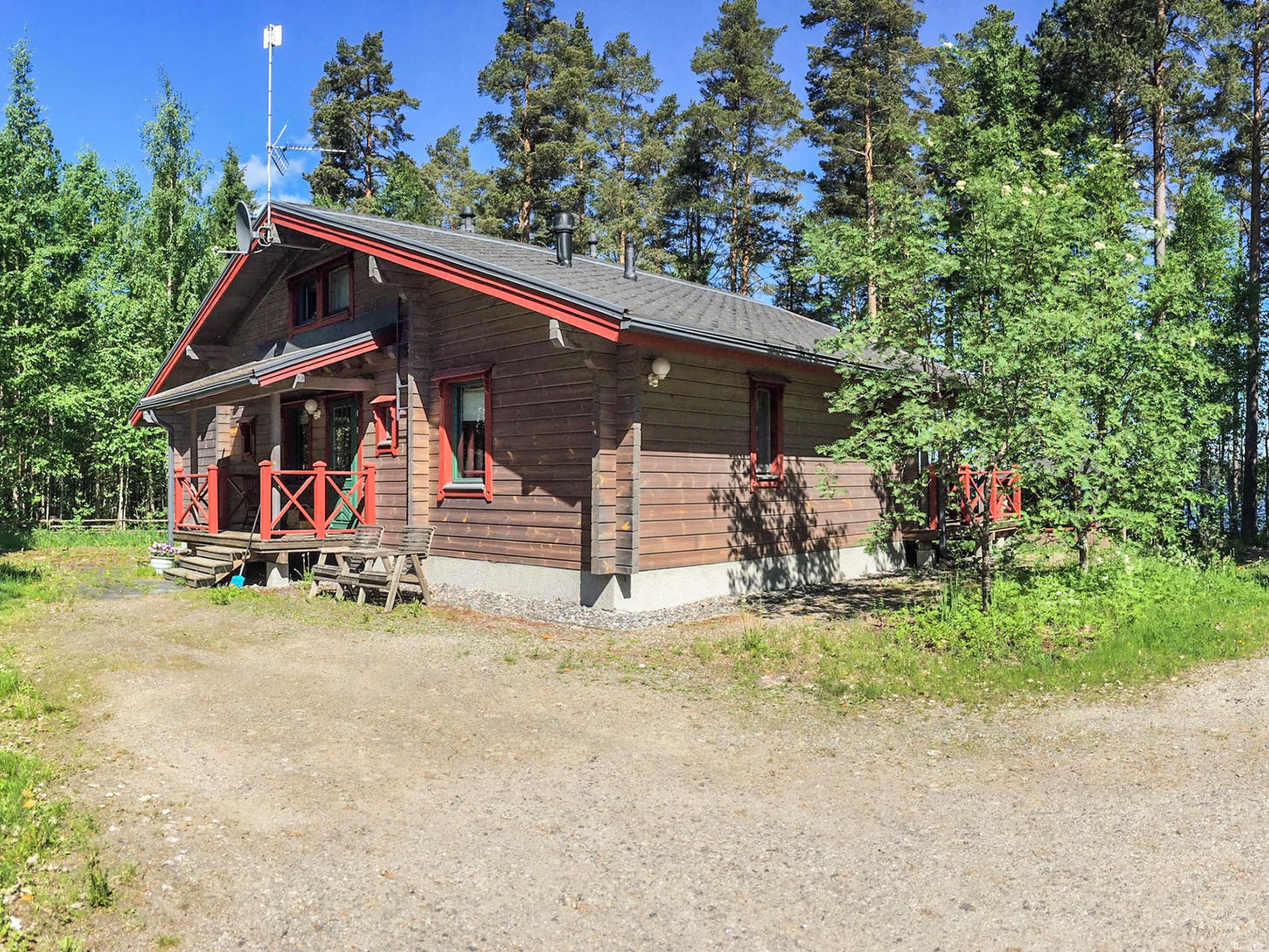 Eine Holzhütte mit Veranda und Schornstein, umgeben von Bäumen.