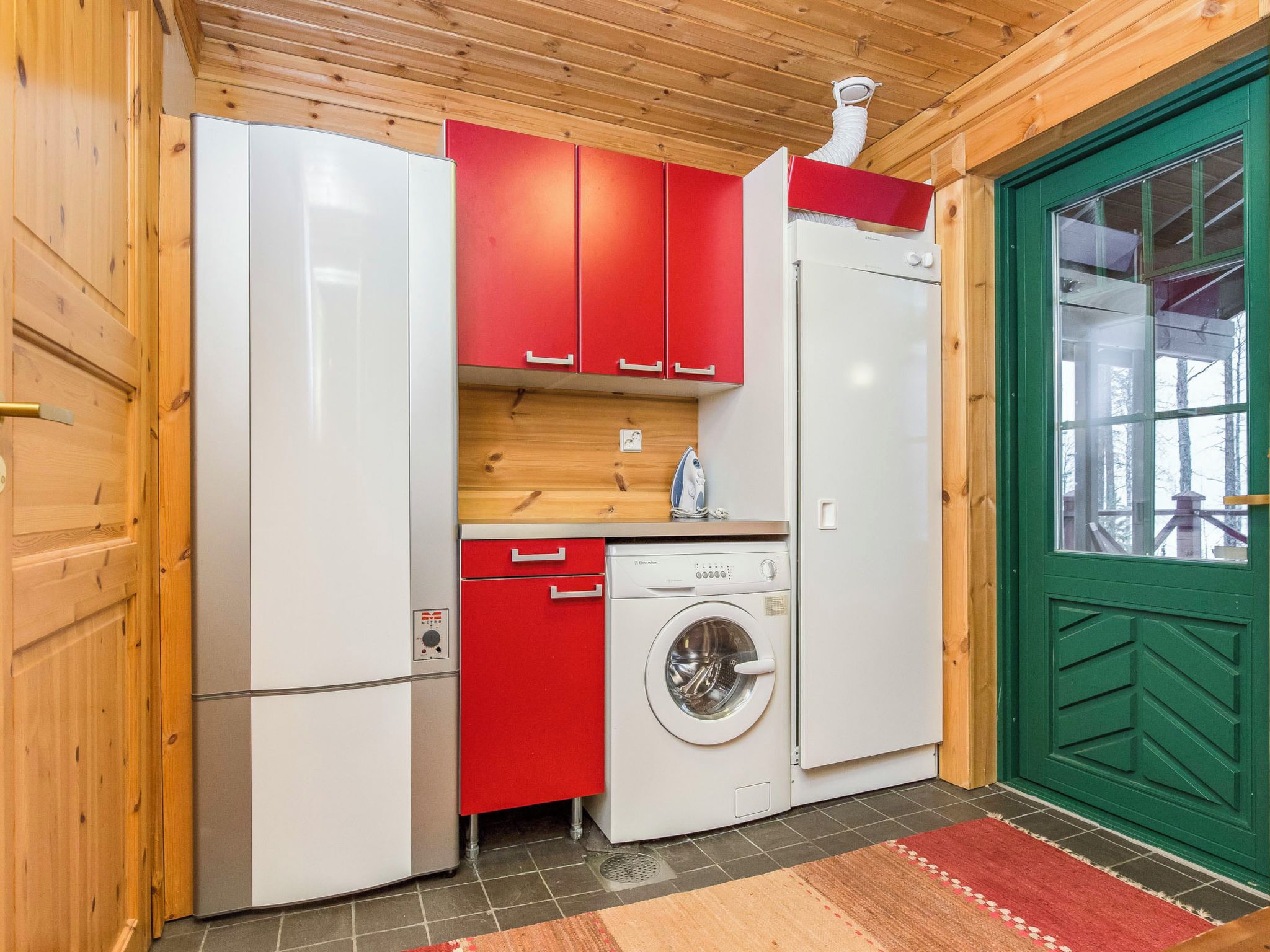 Una cocina funcional con lavadora, refrigerador y una puerta verde.
