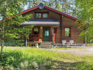 Une cabane en bois à deux étages, avec un toit rouge, une véranda à l’avant dotée de marches et une antenne parabolique.