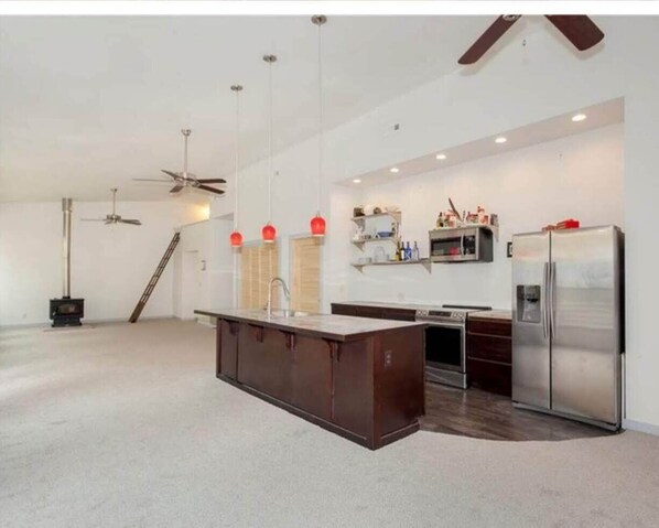 Kitchen features a central island with a sink and oven, two refrigerators, and a dark countertop.