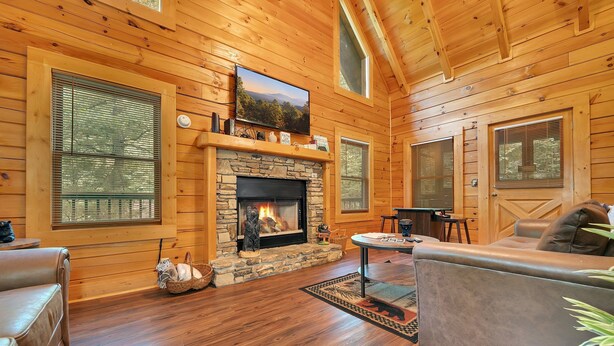 A cozy cabin interior with a stone fireplace, wooden walls, and a comfortable seating area.