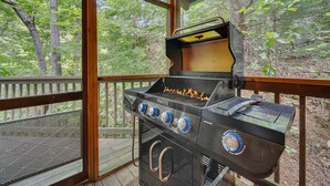 A covered outdoor grill area with a view of a wooded landscape through large windows.