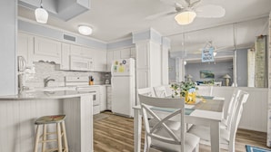 Een moderne keuken met witte kastjes, een centraal eiland en een eetgedeelte met witte stoelen en een tafel.
