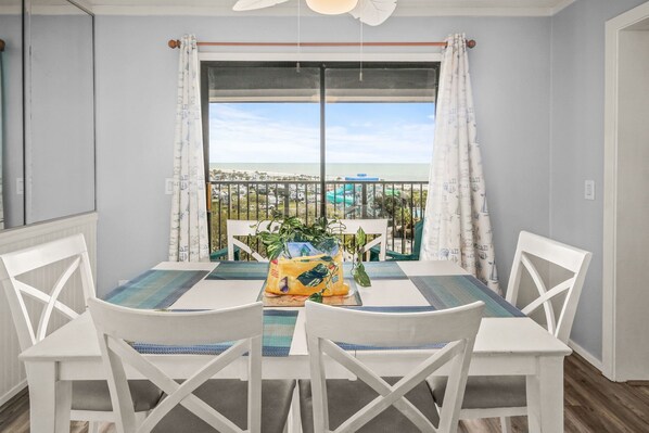A dining area with a table and four chairs, a potted plant, and a view of a water park through a large window.