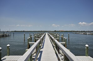 A wooden pier extending into calm water with docks on both sides, leading to a distant shoreline.