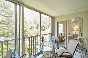 A balcony with a glass table, wicker chairs, and a view of trees.