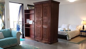 Una habitación con un sofá azul verdoso, un armario de madera, una cama con ropa de cama blanca y una alfombra azul.