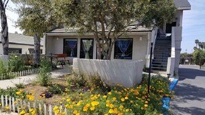 Un edificio con un espacio de estar al aire libre cubierto, una escalera y un jardín con flores amarillas.