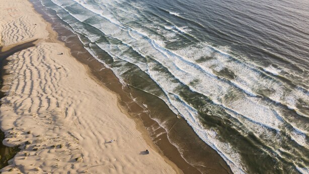 Una playa con olas rompiendo en la orilla, arena dorada y huellas en la arena.
