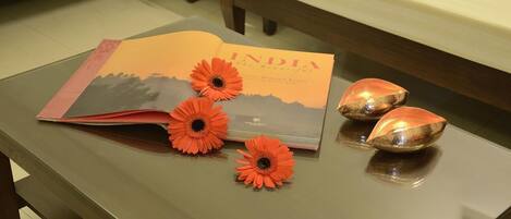 A book titled "INDIA the Beautiful" on a table with three orange flowers and two reflective objects.