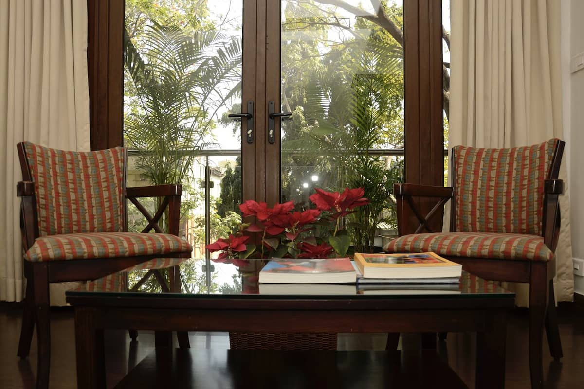 A room with two chairs, a table, and a view of tropical foliage through large windows.