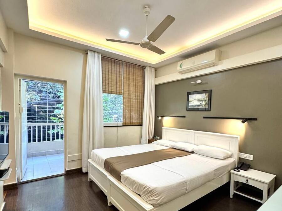 A bedroom with a bed, bedside table, ceiling fan, and a window with curtains.