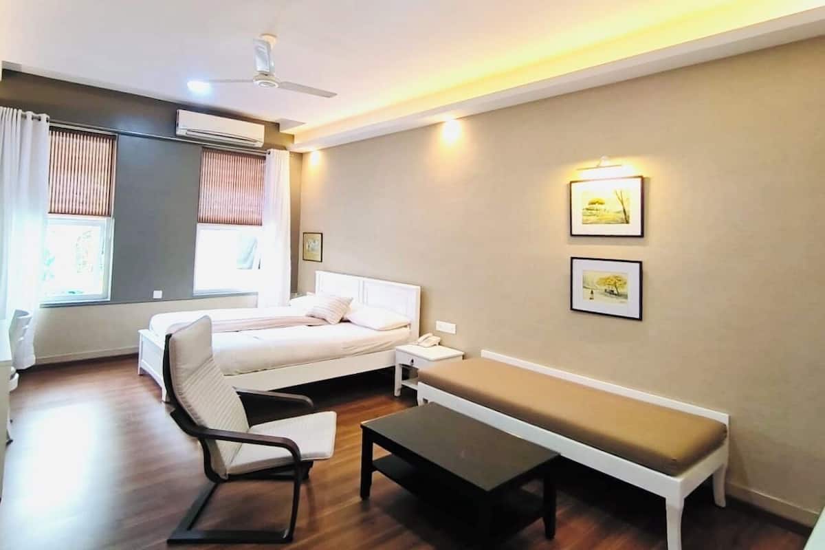 A hotel room with a bed, a desk, a chair, a bench, and two wall-mounted picture frames.