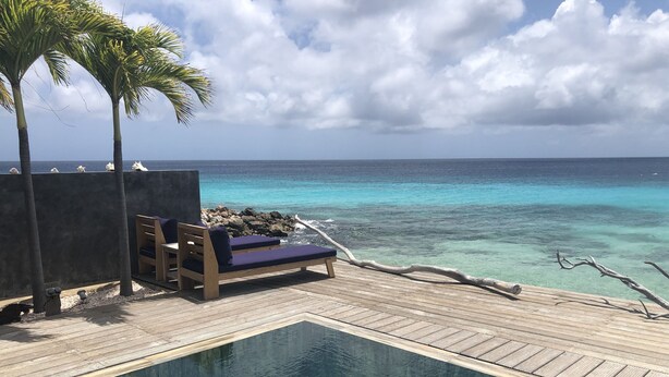 Una piscina a sfioro con terrazza in legno, poltrone relax e vista sull'oceano.