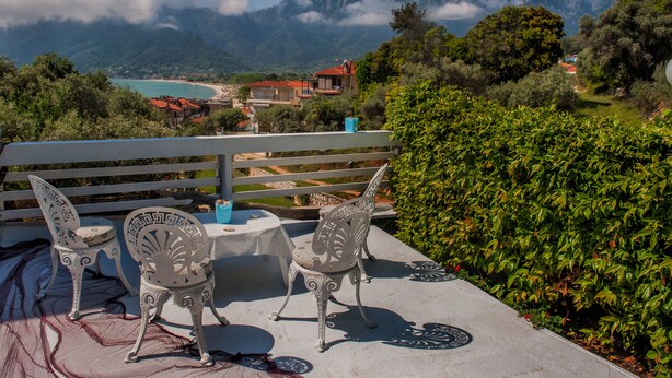 Una terraza con dos sillas ornamentales y una mesa, con vistas a un paisaje costero con montañas y una playa.