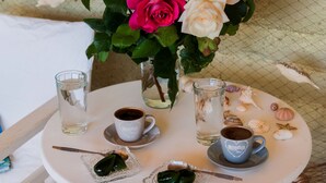 Una mesa redonda blanca con un jarrón de rosas rosadas y blancas, dos vasos de agua, una taza de café y un pequeño plato con un objeto verde.
