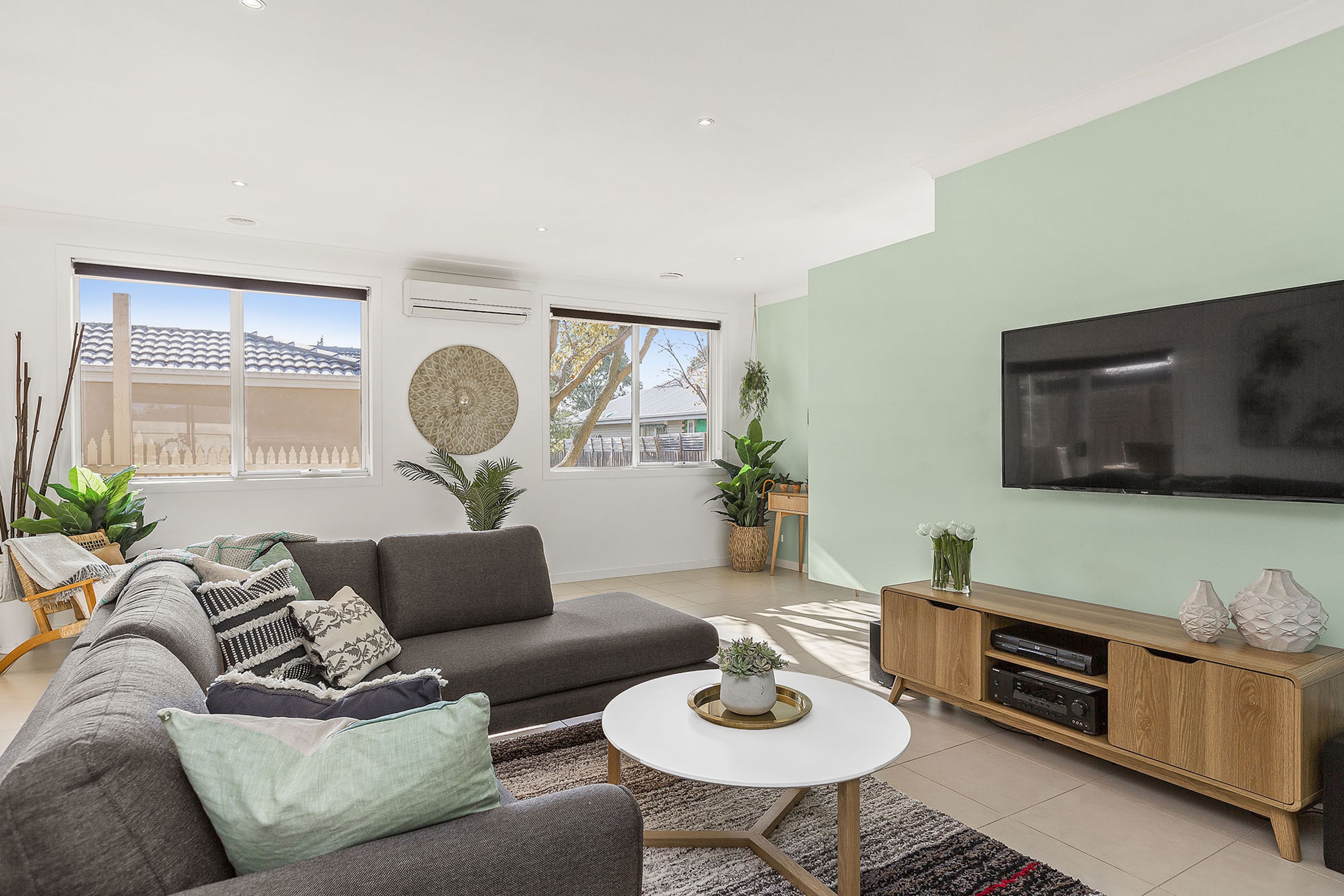 A modern living room with a grey sofa, a coffee table, and a flat-screen TV mounted on the wall.