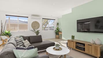 A modern living room with a grey sofa, a coffee table, and a flat-screen TV mounted on the wall.