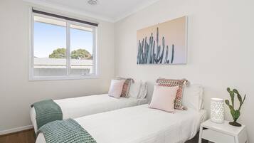 A bedroom with two beds, a window, a painting, and a nightstand with a cactus.