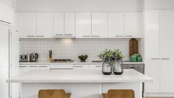 A modern kitchen with white cabinetry, a central island with two wooden chairs, and a Bosch dishwasher.