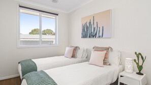 A bedroom with two beds, a window, a painting, a nightstand, and a cactus plant.