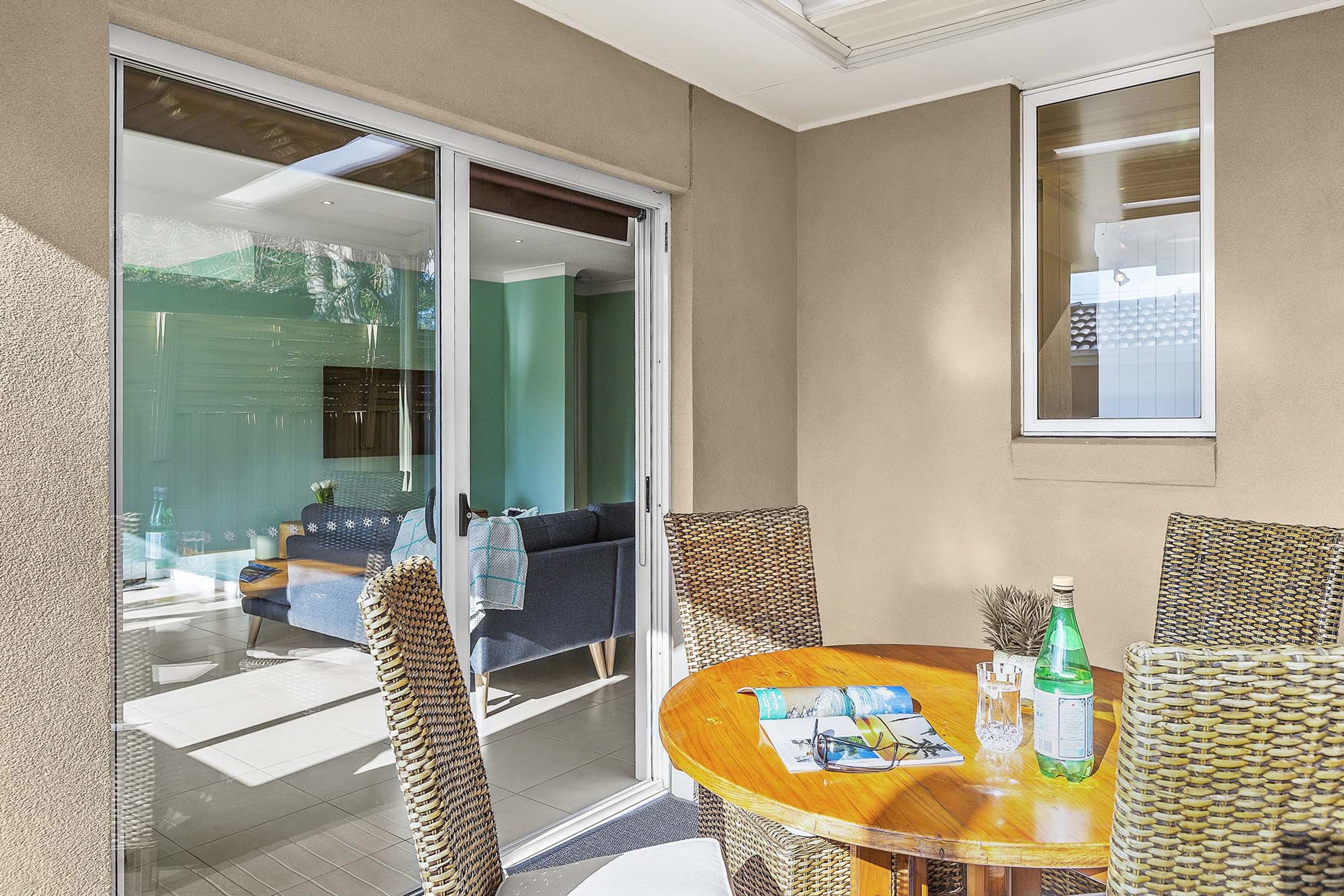 A room with a glass door leading to a balcony, a round wooden table with chairs, and a bottle of water.