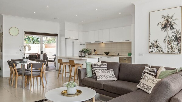 A modern living room with a grey sofa, a coffee table, and a dining area with wooden chairs and a glass table.