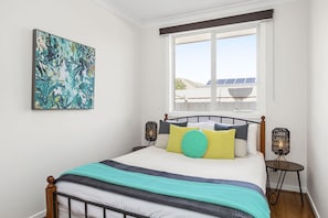 A bedroom with a bed, a window, a wall-mounted artwork, and a nightstand with a lamp. - The Richardson a  Dendy Apartment with Garage (Mentone)
