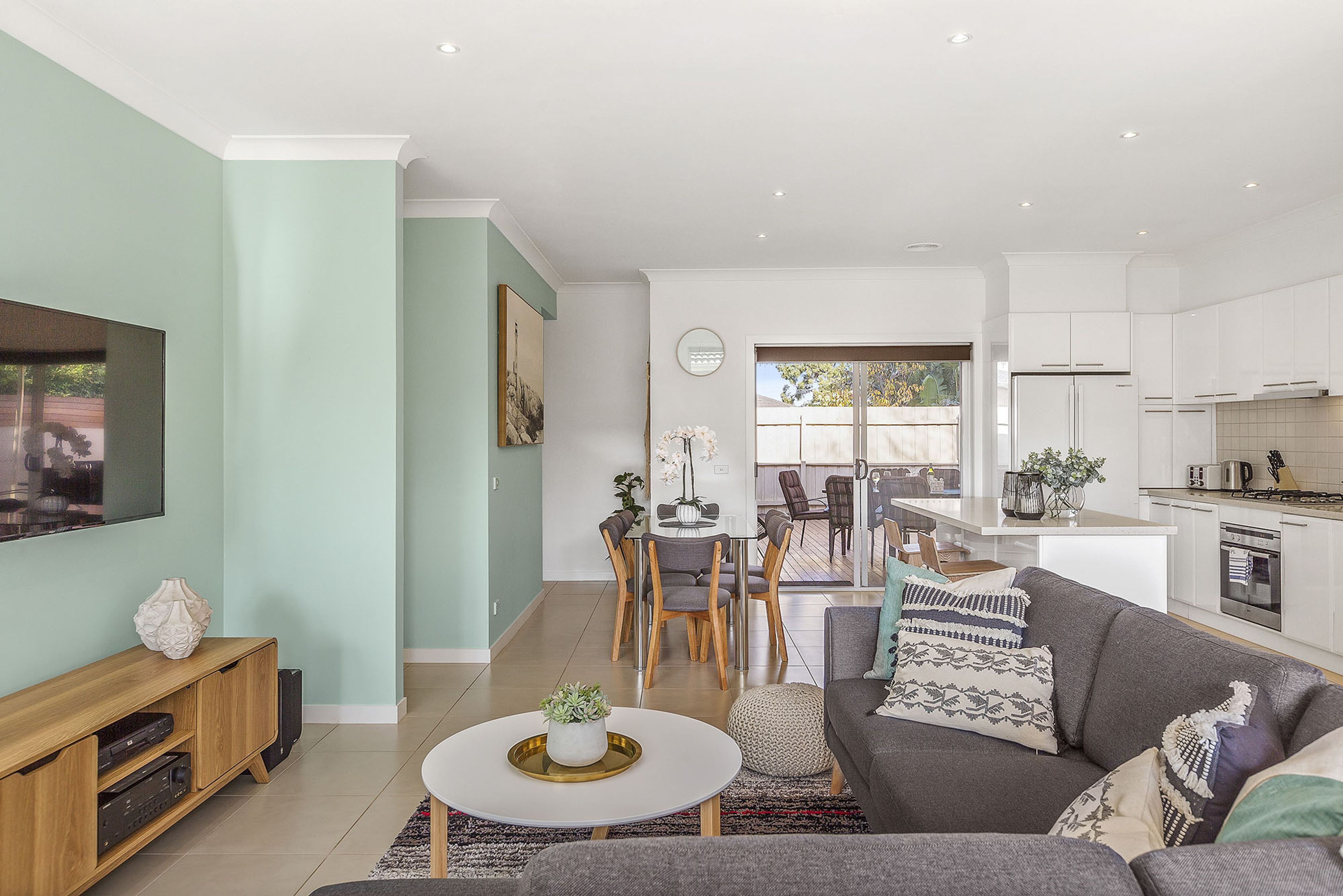 A modern living room with a flat-screen TV, a sofa, and a dining area with chairs and a table.
