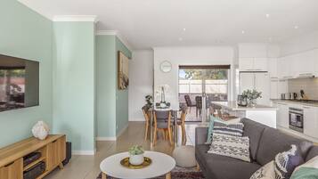 A modern living room with a flat-screen TV, a sofa, and a dining area with chairs and a table.