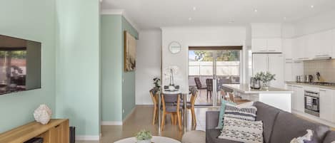 A modern living room with a flat-screen TV, a sofa, and a dining area with chairs and a table.