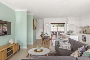 A modern living room with a flat-screen TV, a sofa, and a dining area with chairs and a table.