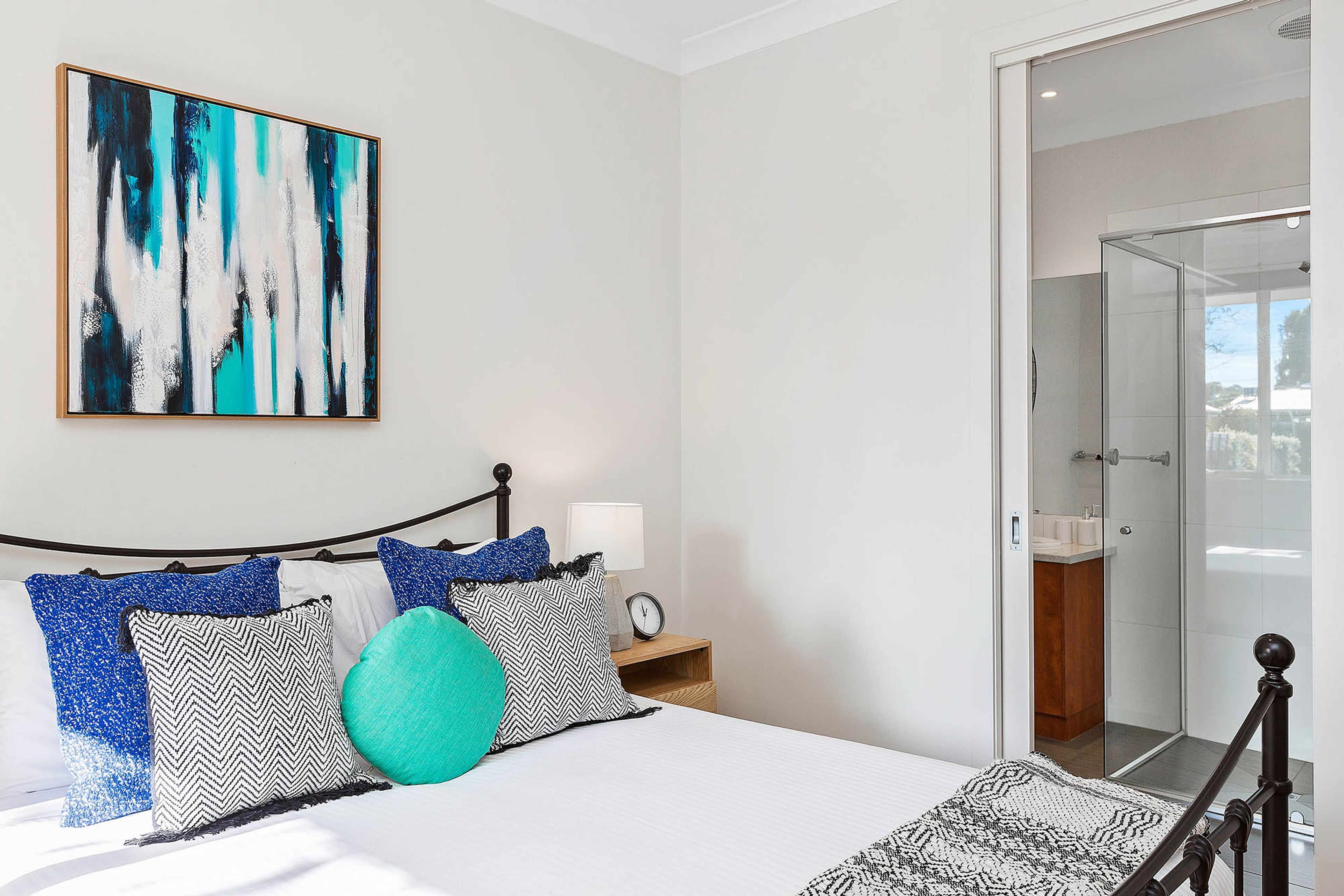 A modern bedroom with a bed, a bedside table with a lamp, and a large abstract painting on the wall.