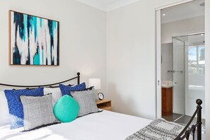 A modern bedroom with a bed, a bedside table with a lamp, and a large abstract painting on the wall. - The Richardson a  Dendy Apartment with Garage (Mentone)