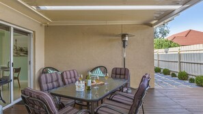 An outdoor patio with a glass-top table surrounded by cushioned chairs, a wine bottle, and glasses.