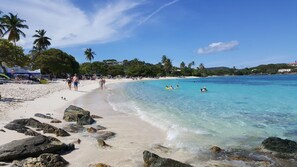 A beach with clear turquoise water, white sand, and rocky outcrops.