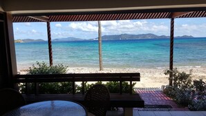 A beach view from a covered outdoor seating area with a table and chairs. - Scenic Ocean front walk-out~fully renovated~property wide generators  (St Thomas, USVI)