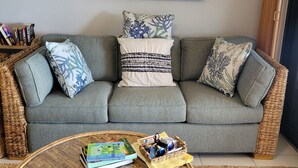A living room with a grey sofa, a woven coffee table, and a painting above the sofa. - Scenic Ocean front walk-out~fully renovated~property wide generators  (St Thomas, USVI)