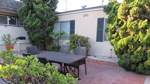 Un patio con una mesa y sillas, rodeado de plantas en macetas y un muro de ladrillo.
