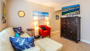 Una sala de estar con un sofá color beige, un sillón rojo, un aparador de madera y un televisor grande en la pared.
