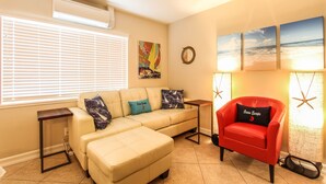 Una sala de estar con un sofá seccional color beige, un sillón rojo, una mesita auxiliar y un espejo fijado a la pared.