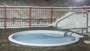An outdoor swimming pool with a red metal fence, surrounded by snow-covered ground and a tree. - Ski In/Ski Out Modern Condo in Wildwood  at Creekside (Vernon)