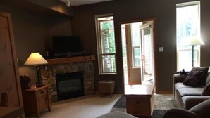 A living room with a fireplace, a television, and a sofa. - Ski In/Ski Out Modern Condo in Wildwood  at Creekside (Vernon)