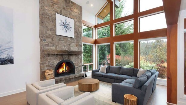 A modern living room with a stone fireplace, large windows, and a sectional sofa. - Luxury golf course chalet with hot tub (Whistler)