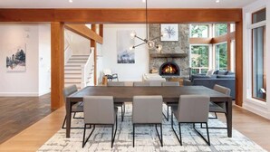 A spacious dining area with a long table, chairs, a fireplace, and a staircase leading to another level. - Luxury golf course chalet with hot tub (Whistler)
