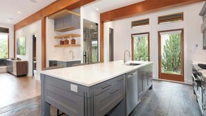 A modern kitchen with a central island, built-in appliances, and large windows. - Luxury golf course chalet with hot tub (Whistler)