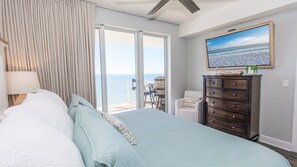 Ein Schlafzimmer mit Bett, Kommode, Stuhl und einem großen Fenster mit Meerblick.