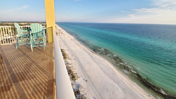Un balcon avec des chaises turquoise et une vue sur une plage et l’océan.