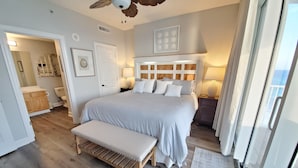Une chambre dotée d’un grand lit, d’un plancher en bois, d’un ventilateur de plafond et offrant une vue sur l’océan grâce à une porte coulissante.